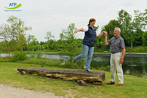 2 ältere Menschen balancieren auf einem Baumstamm