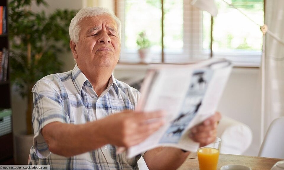 Älterer Mann hält Zeitung von sich weg, um Schrift zu erkennen