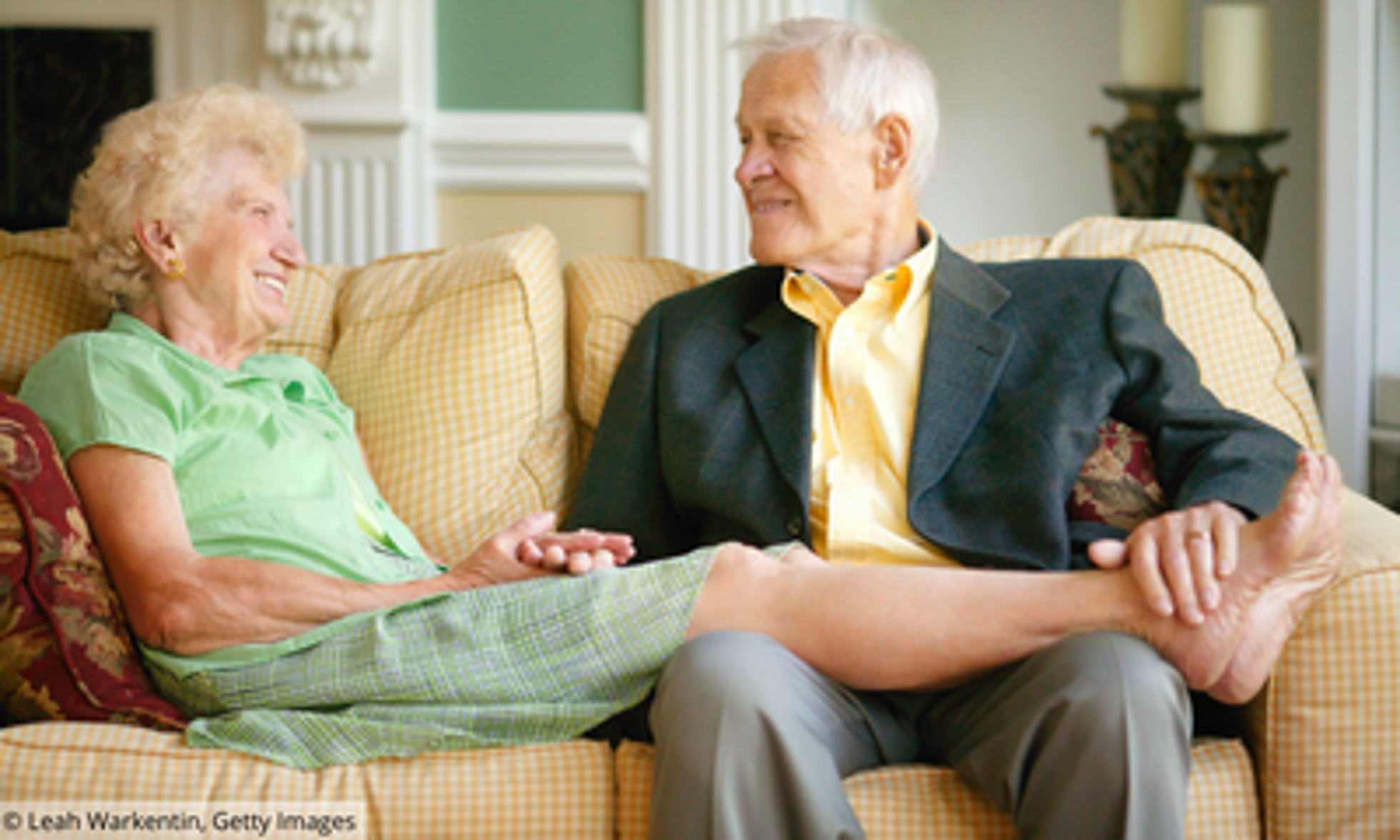 Älterer Mann und ältere Frau sitzen auf dem Sofa und sie hat ihre Beine auf seinen Schoß gelegt