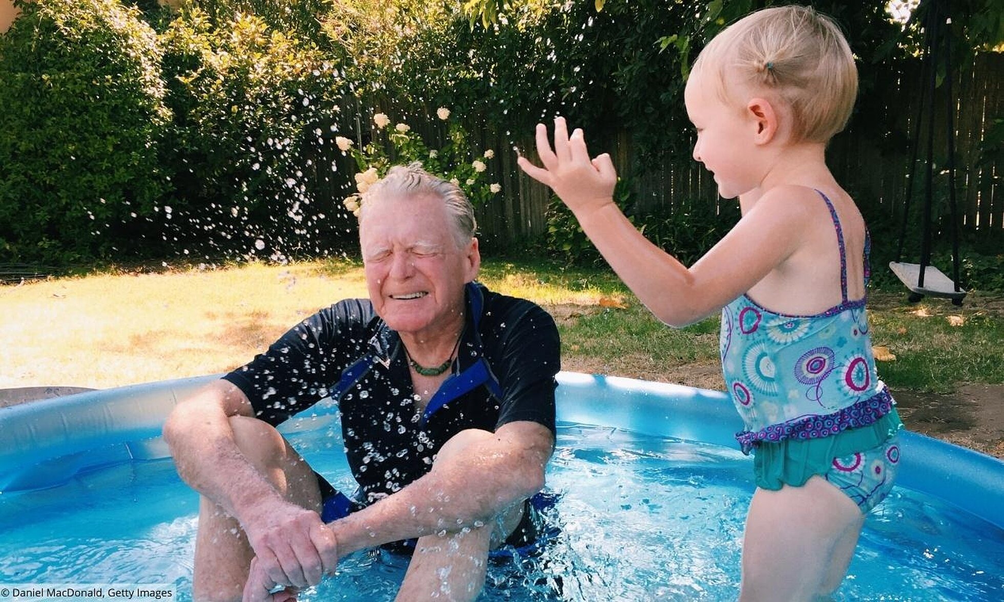 Älterer Mann mit Kind im Pool wird nass gespritzt