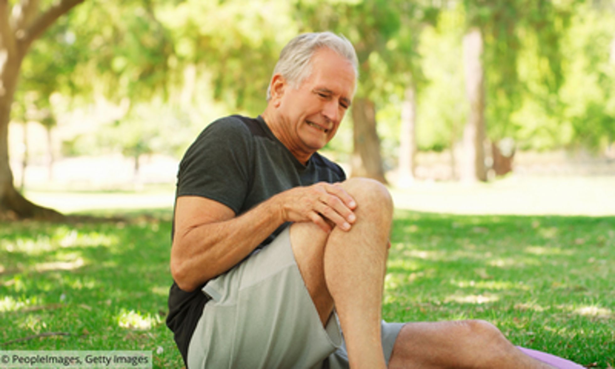 alter Mann sitzt im Park auf dem Boden und hält sein Knie mit schmerzverzerrtem Gesicht