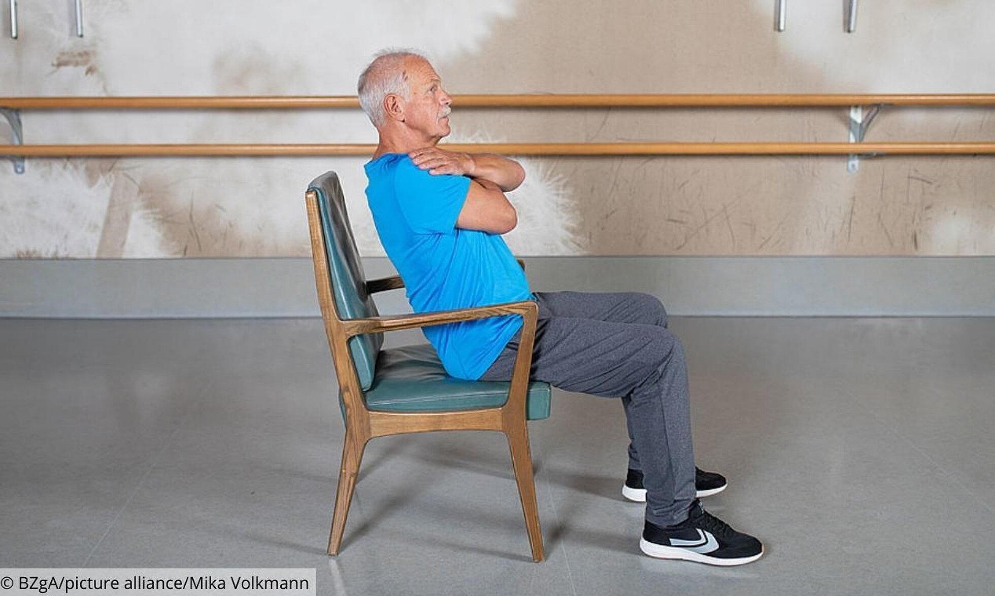 Älterer Mann bei Übung zur Kräftigung der Bauchmuskeln sitzend auf einem Stuhl