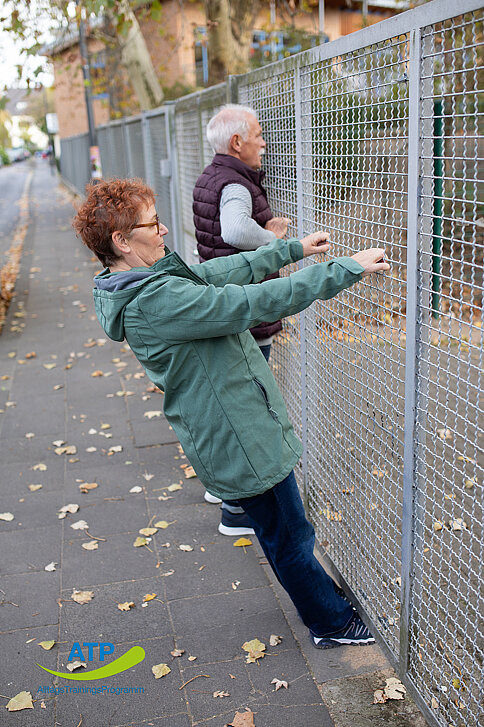 Ältere Frau bei Ruderbewegung an einem Zaun